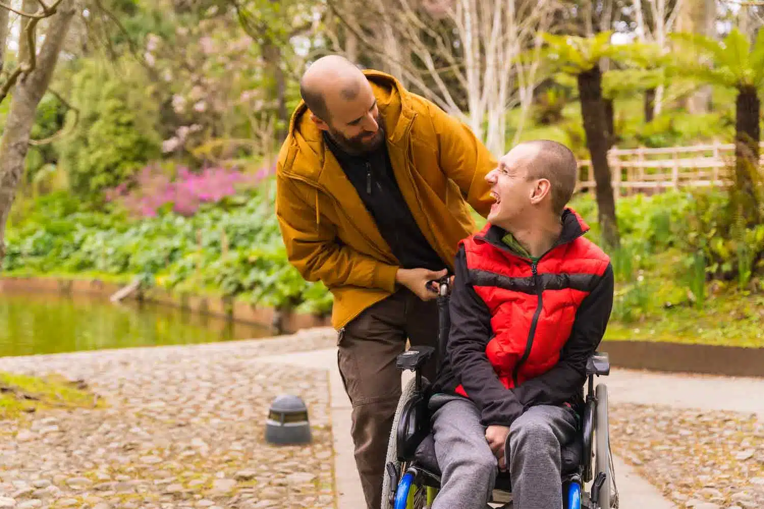 Deux hommes se regardent et sourient. L'un des deux est sur un fauteuil roulant.